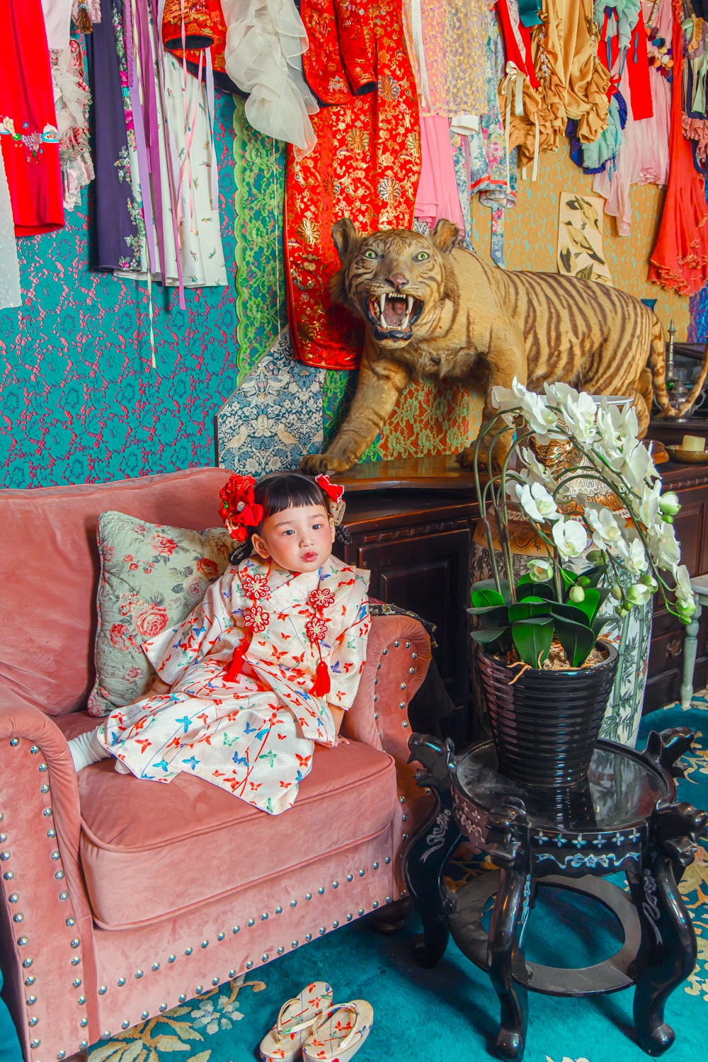 蝶柄の着物に赤い髪飾りを合わせ、ピンクの椅子に座るお子さま